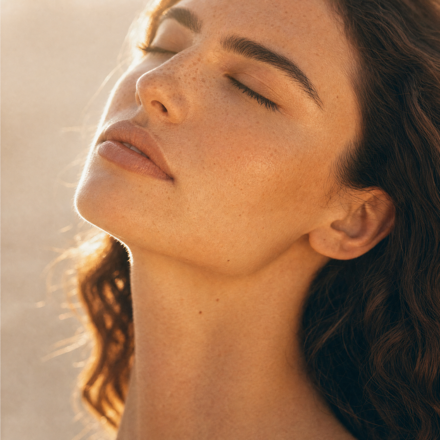 A woman's face in warm golden light, eyes closed and chin lifted, skin the subject